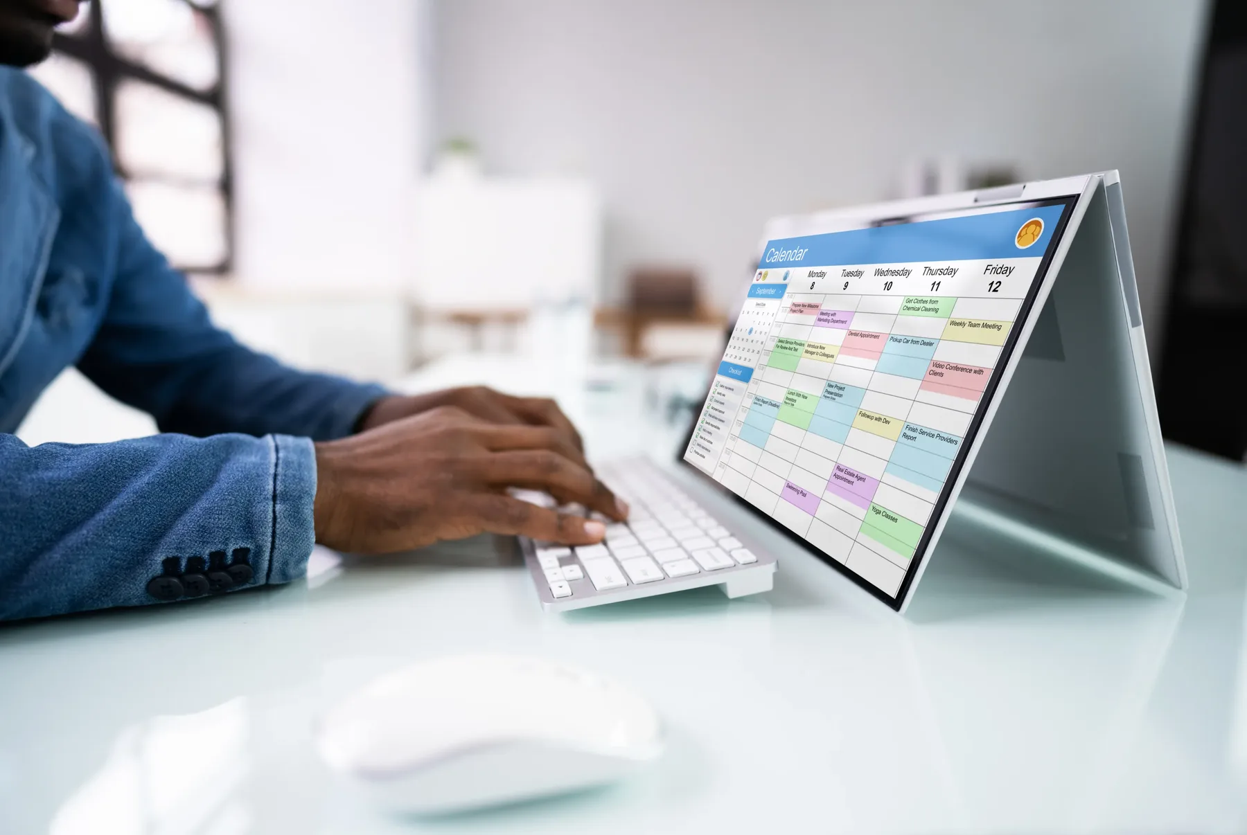 A person reviewing a weekly calendar on a laptop screen at a bright desk.